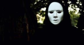 A hooded figure wearing a white mask