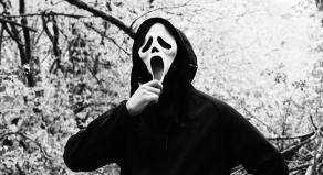 Black and white photo of someone wearing the Scream ghost faced killer costume