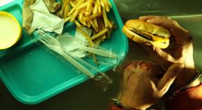 A handcuffed man with bloody knuckles holds a cheeseburger and french fries