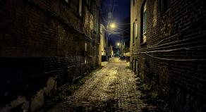 Dark and eerie urban city cobblestone brick paved alley at night