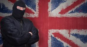 A man in a balaclava stands in front of a British flag