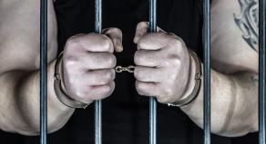 A criminal stands handcuffed in prison