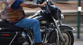 A man in jeans and a biker vest rides a Harley Davidson bike