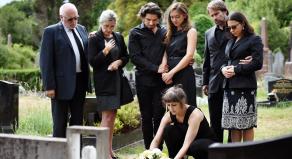Seven family members dressed in black look solemn as they lay a wreath of flowers on a grave