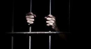 A stock image of a person holding onto jail bars