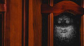 The outline of a face can be seen on the other side of a frosted glass door