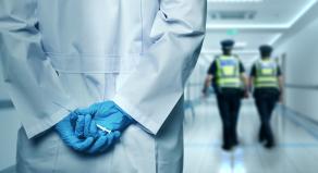 A stock image showing a person holding a syringe whilst police are in the distance