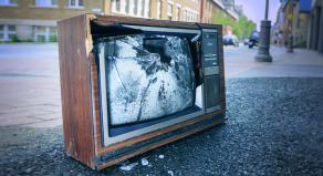 A photograph of a broken TV set discarded at the side of a street