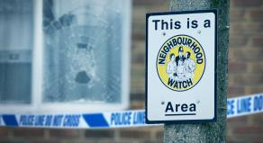 A stock image of a smashed window in front of a Neighbourhood Watch sign