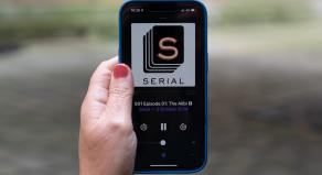 A person holding a mobile phone with the Serial podcast logo displayed on the screen