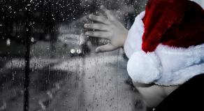 A boy wearing a santa hat looking out of a rainy window