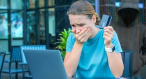 A woman holding a credit card holds her mouth in shock while browsing the internet