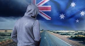 A hooded figure on a road in the outback. The Australian flag in the sky