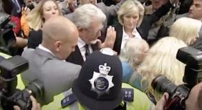 Rolf Harris walking out of court through a melee of police and journalists