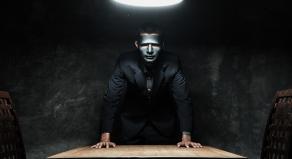 A man with a black mask standing over a desk