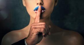 A man pressing his finger against a woman's lips to 'shush' her