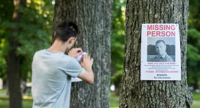 A man pinning 'Missing Person' posters to trees