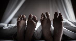 Two pairs of feet stick out the bottom of a duvet