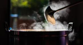 A ladle is used in a large pot which is steaming