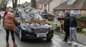 Members of the public place red roses on a hearse