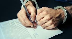 A man signing a document while wearing handcuffs