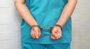 A person wearing medical scrubs with their hands cuffed behind their back