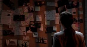 A female detective looking at a criminal investigation evidence board
