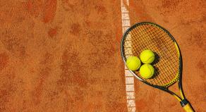 Three tennis balls and a tennis racquet lie on a clay tennis court