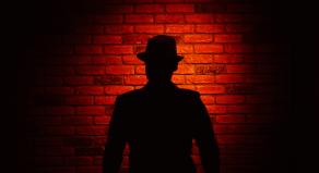 Silhouette of a man wearing a fedora on a red brick background