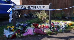 Floral tributes are left under a road sign for 'Ashlyn Close' that is also covered in police tape