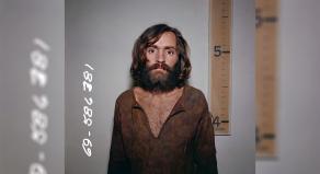 Charles Manson mugshot in front of a height chart that shows him to be a few inches taller than five foot