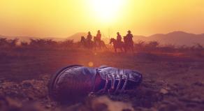 Men on horseback overlook a discarded boot in the Texas desert