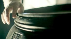 A person with a latex glove on sealing the lid of a large plastic barrel
