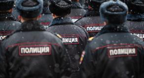 Multiple lines of Russian police officers face away from the camera as light snow falls on them