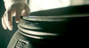 A person with a latex glove on sealing the lid of a large plastic barrel