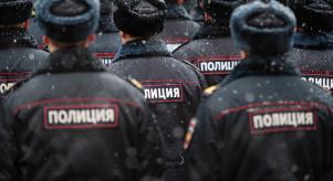 Multiple lines of Russian police officers face away from the camera as light snow falls on them