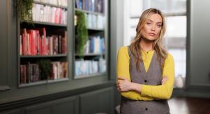 Laura Whitmore standing with her arms crossed in front of a large bookcase