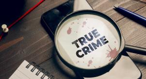 A magnifying glass lying on a smartphone with the words 'True Crime' written on the screen