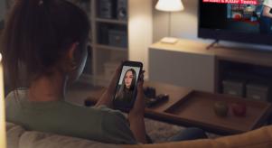 A woman looks at an image of True Crime Caitlyn on her phone while 'Laura Whitmore on Britain's Killer Teens' plays on her television