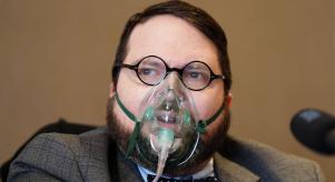 Nicholas Rossi (Alahverdian) speaking at a press conference while wearing an oxygen mask