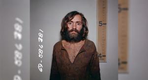 Charles Manson mugshot in front of a height chart that shows him to be a few inches taller than five foot