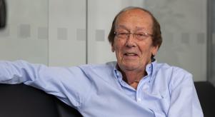 Fred Dinenage sitting with his arm up on a sofa wearing a blue shirt