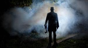 Silhouette of a man standing in a dark and smoky forest holding an axe
