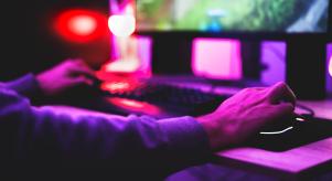 Someone using a PC set up to play an online game with purple lights shining on them