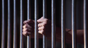 A man holding onto the bars of a prison