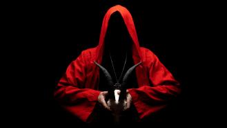 Man in red ritual hooded cloak holds a skull with horns in hands