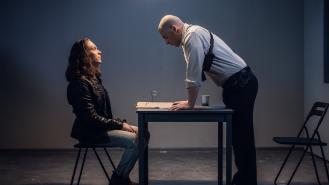 A policeman charges a man detained in handcuffs while inside an interrogation room.