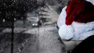 A boy wearing a santa hat looking out of a rainy window