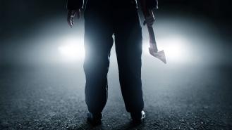 A man holds an axe in front of car headlights