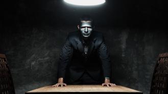 A man with a black mask standing over a desk